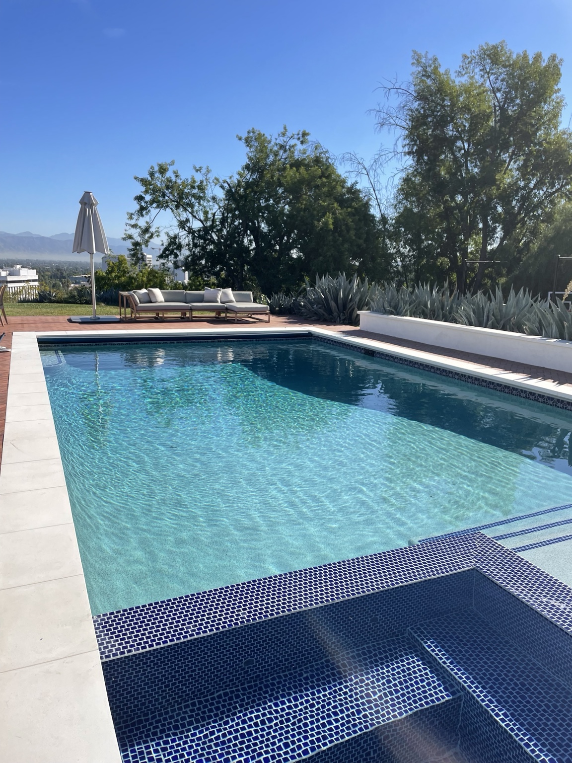 Bright rectangular swimming pool with blue tile spa and sunny hillside view